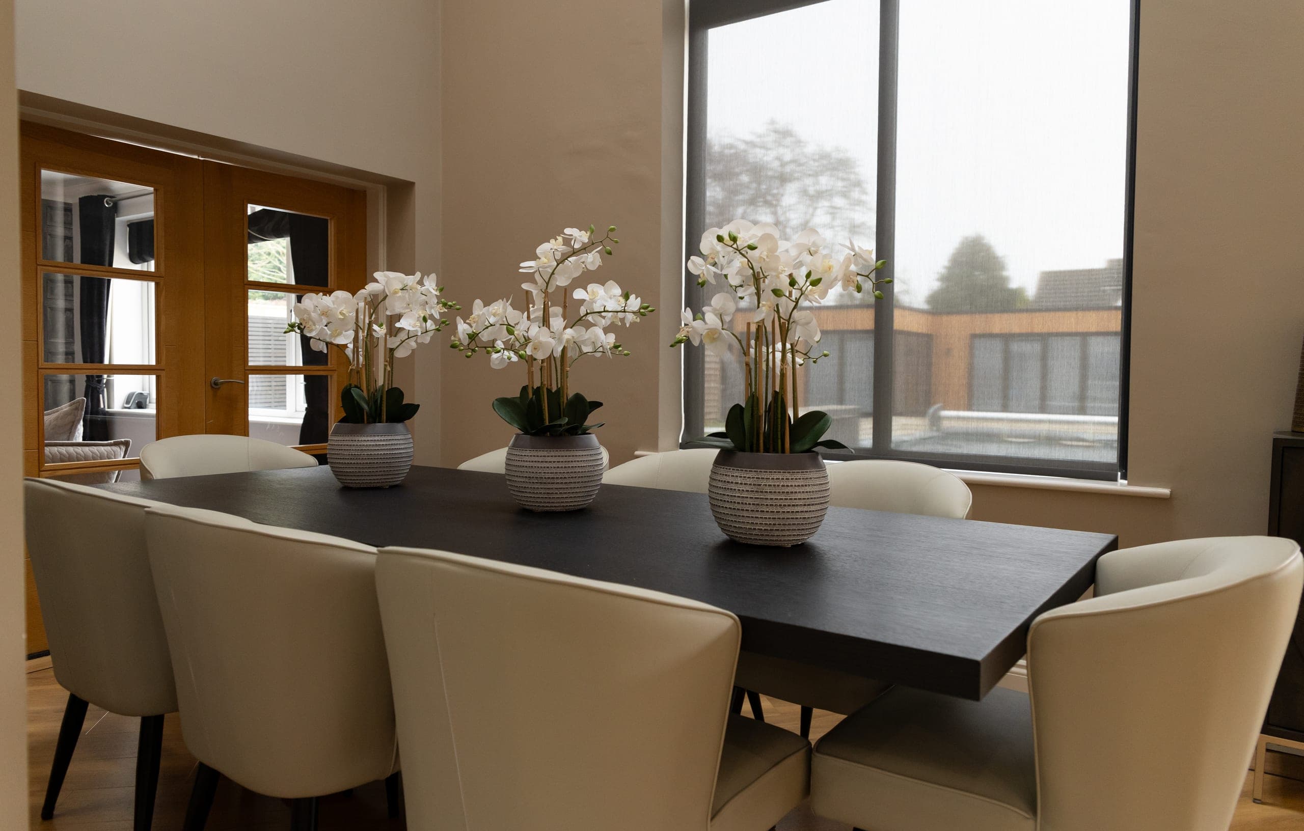The dining room, with a long dark table, cream chairs and white orchids, and garden views through the window
