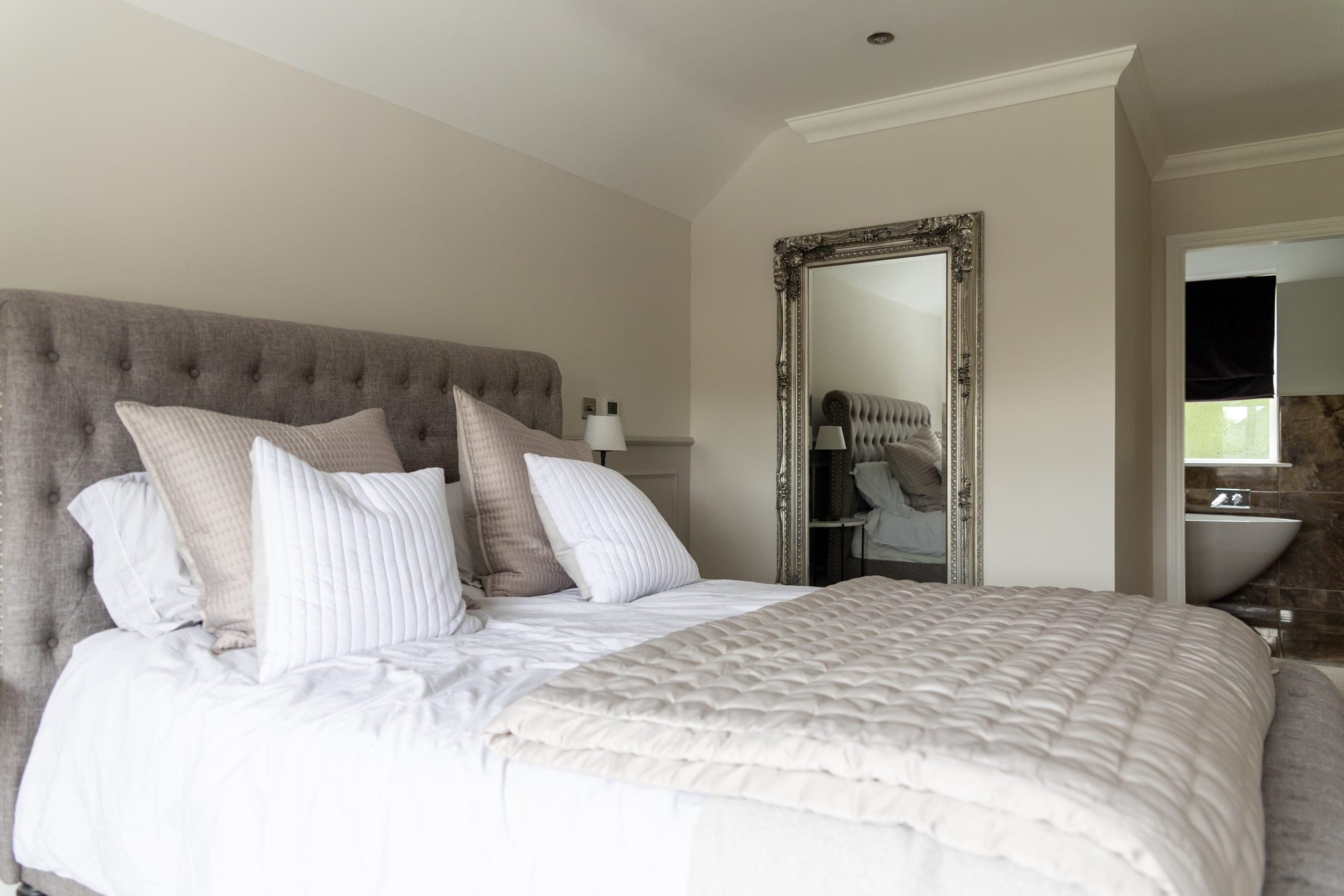 The master bedroom, with a large upholstered bed and soft grey linen